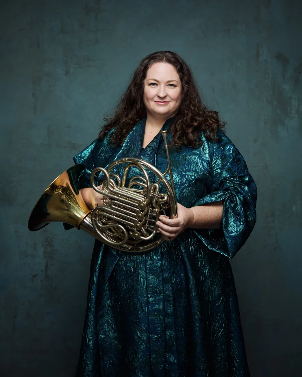 Megan Cullen holding her horn against a teal backdrop
